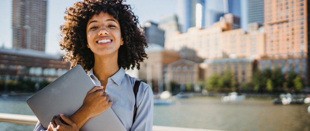 Young woman holding a laptop and smiling, confident about her IT career path